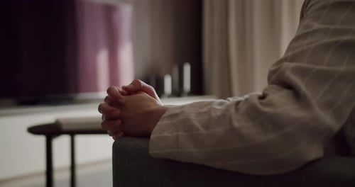 Person Sitting on Chair with Clasped Hands in Living Room Setting