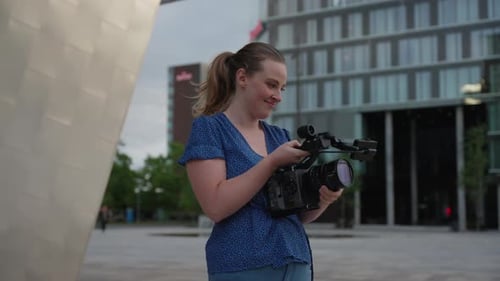 Young Woman Adjusting Professional Video Camera Outdoors