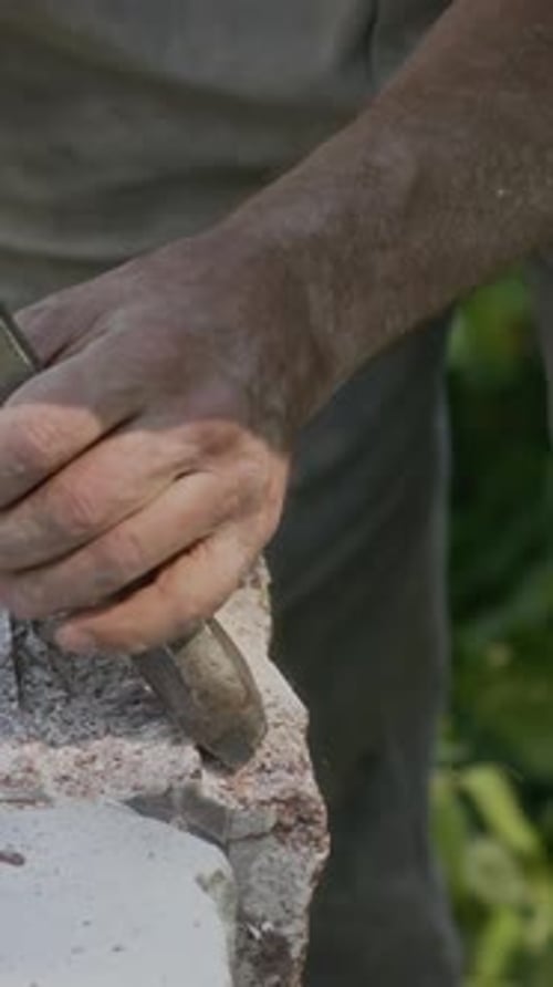 Vertical of Sculptor Using Chisel and Hammer to Carve Piece of Stone