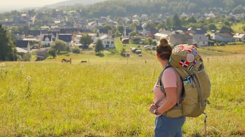 Walking backpacking traveler looking out past a grassy meadow to a small German town in the distance