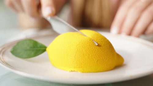 Eine Frau schneidet langsam ein Zitronenmousse-Dessert in zwei Hälften, Nahaufnahme.