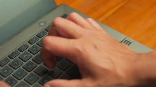 Close Up of Professional Hands Typing on Laptop Keyboard at Wooden Desk
