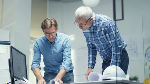 Two Senior Engineers Work with Schemes and Blueprints while Standing over Working Table. They have