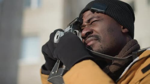 Side View Man Adjusting Camera Lens on Snowy Street Under Sunny Sky