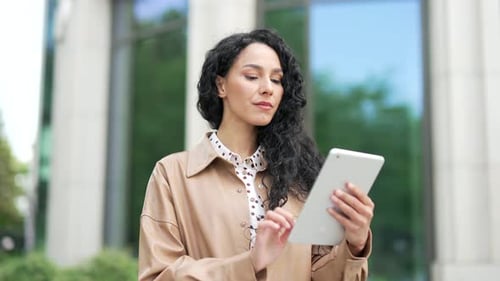 Close up. Young confident businesswoman is using a tablet while standing on the street near