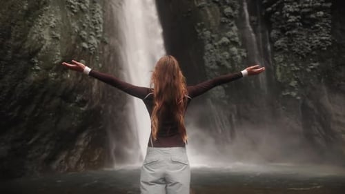 Woman enjoying waterfall in nature with outstretched arms