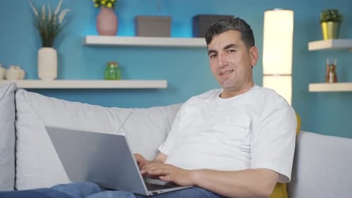 Man Smiling and Using Laptop on Gray Couch