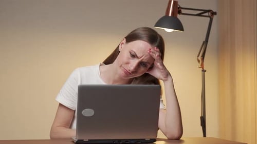 Tired Young Business Woman or a Student with a Headache Using a Laptop in a Home Office