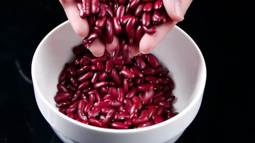 Hands Pouring Red Kidney Beans into White Bowl