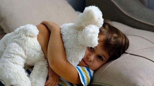 Child Lying on Couch Hugging a Stuffed Animal