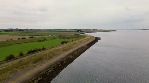 Un paysage côtier calme avec des champs verdoyants, des sentiers sinueux et une digue le long du rivage, capturé