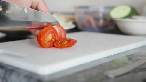 Cooking, I cut the tomato into thin slices with a large knife, close-up in motion. Black stone count