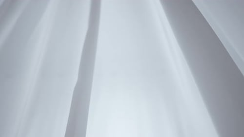 Transparent White Silk Fabrics Floating From an Open Window with Soft Light Shining Through Shadows