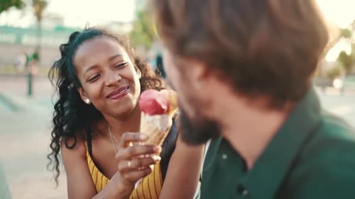 Closeup of smiling interracial couple eating ice cream in urban city background