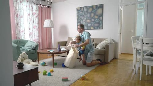 Der Vater putzt im Wohnzimmer mit seinem Säuglingsbaby im Tragetuch