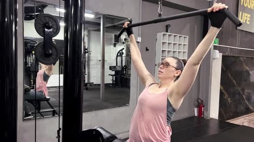 Frau mit Brille trainiert mit Klimmzug im Fitnessstudio, Trainingsbewegungen für die Armmuskulatur
