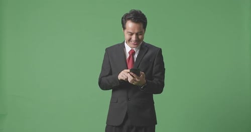 An Asian Business Man Enjoy Using Mobile Phone While Standing On Green Screen In The Studio