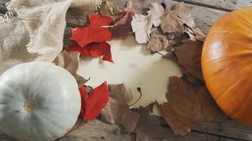 Paper with copy space against autumn leaves and pumpkins on wooden surface