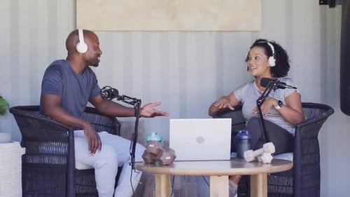 Coanimateurs afro-américains, homme apprenant, commençant à discuter, parlant, faisant des gestes en studio avec micros, ordinateur portable