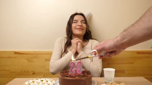 30sm. The girl is sitting in front of a table with a festive cake, in which a candle in the form of