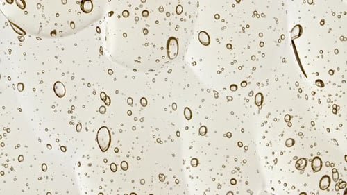 Gel cosmético transparente amarillo con burbujas moleculares que fluyen sobre la superficie blanca lisa