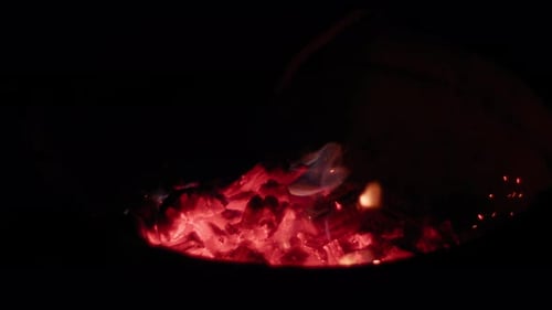 Glowing hot wood coals being preped by a male hand in slow motion. Filmed with a Blackmagic Pocket C