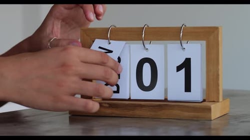 Man's Hands Turn Over the Paper Pendant Calendar on the Marble Table Against White Wall Background