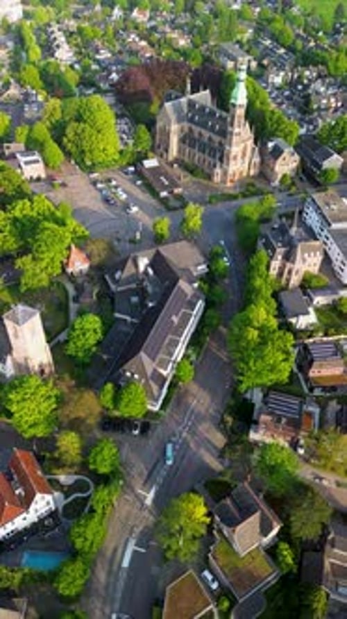 Aerial drone view of a town square with a parking lot, cars, trees, and geometric patterns