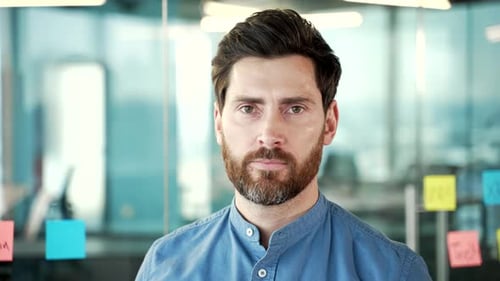 Portrait of a serious bearded manager in a shirt standing at the workplace in a business office.
