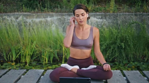 Woman Meditating Outdoors with Tablet and Earbuds