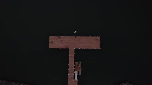Drone top down ascend above T shaped wooden dock pier with fishermen along boardwalk with homes