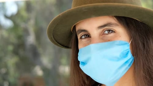 portrait of beautiful girl with hat and medical face mask . brown eyes. looking at camera on green b
