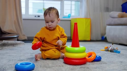 One year old toddler in orange suit playing with a pyramid.