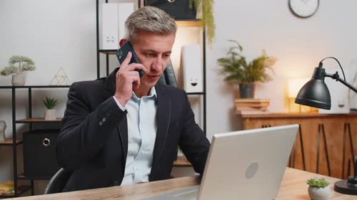 Confident Young Entrepreneur Using Laptop and Smartphone While Working on Project at Home Office