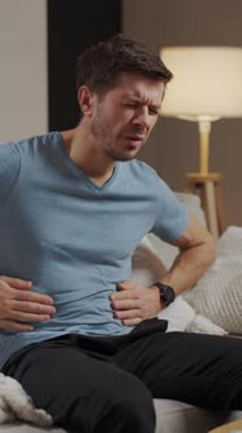 Adult man experiencing stomach pain while sitting on couch