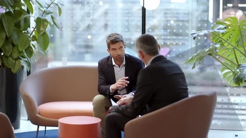 Two talking businessmen sitting in office lounge