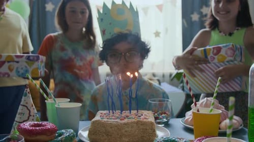 Boy with Paper Crown Blowing out Candles on Cake, Friends Clapping Hands