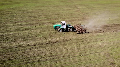 Aerial Drone View of Farmer on Green Wheeled Tractor with Cultivator Plowing Soil in Field