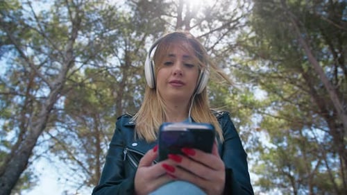 Woman with Headphones Using Phone Outdoors in Park