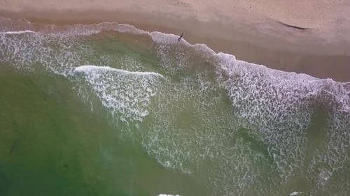 A woman stands on an empty beach as the waves roll towards her.