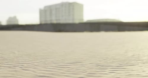 Waves of Sand Ripple Under Sunlight on a Beach Near Buildings at Dusk