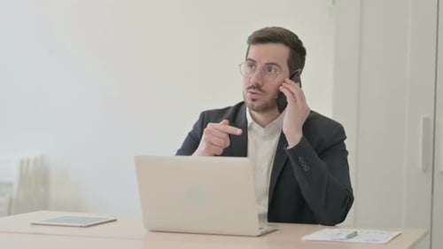 Man in Suit Talking on Phone, Frustrated at Desk