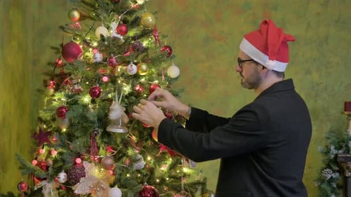 Man Decorating Christmas Tree Wearing a Santa Hat