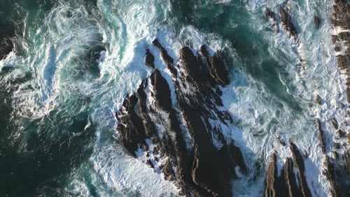 Ocean waves on rocky coast, top down aerial drone view of rough sea water surface