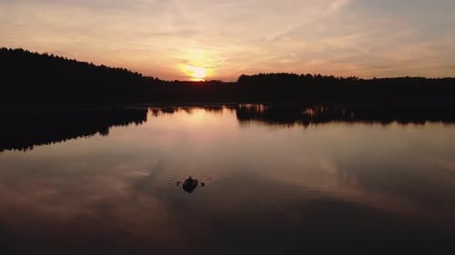 Beautiful Sunset And Calmness Of A Lake With Person Paddling A Rubber Boat During Summer Evening In