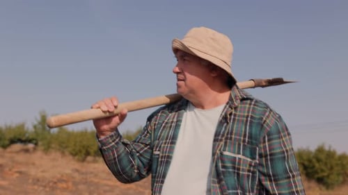 Hardworking Senior Embarks on Field Work with Shovel Front View and Tracking Shot of a