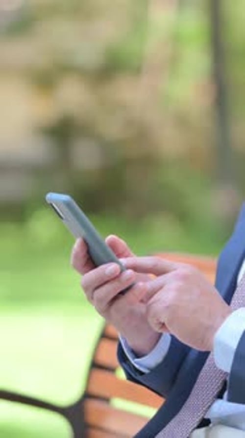 Side View of Businessman using Smartphone sitting Outside Office, vertical