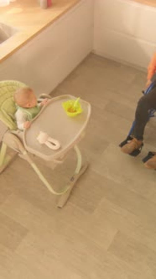 Man Feeds Infant in Highchair in Kitchen