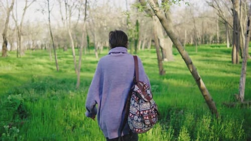 Woman Walks Through a Green Field Surrounded By Trees During a Sunny Day in an Outdoor Park in