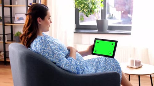 Pregnant woman at home waves hand during video call on tablet with green screen